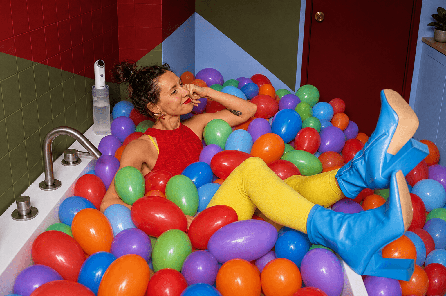 Woman relaxing in a bathtub full of colourful balls, Electric Moley on the edge